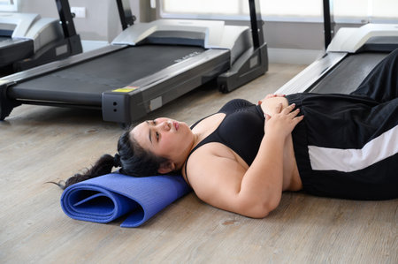 Exhausted woman lying on yoga mat after training in gym. Young woman hard work to lose weight....