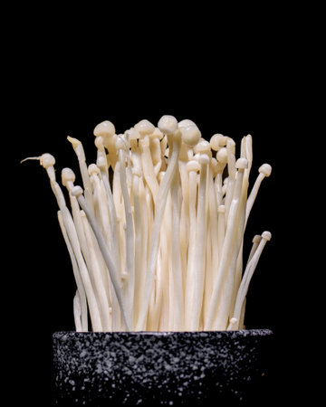 A bunch of white mushrooms are in a black bowl. The mushrooms are small and white, and they are arranged in a way that they are all facing the same directionの写真素材