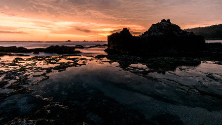 Dramatic sunset sky with vibrant clouds and big rock formations as silhouettes. Perfect for nature, weather, and atmospheric conceptsの写真素材