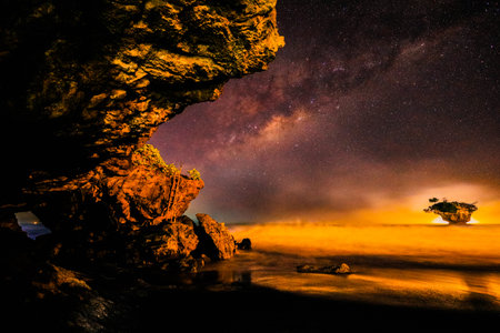 A mesmerizing night scene features a starry sky with the Milky Way. A rugged hole on the left frames the dramatic seascape.の写真素材