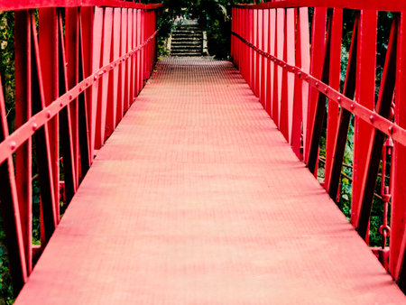 Vibrant red suspension bridge stretching through lush green foliage, leading to a distant stairway...