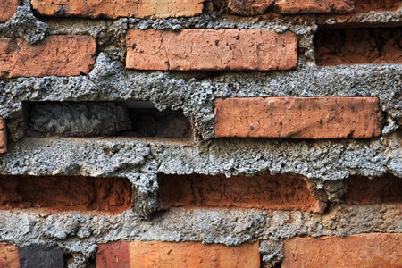A close-up of an old, weathered brick wall with missing bricks and rough, crumbling mortar,...