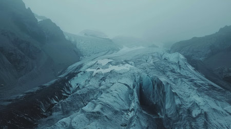 Aerial view of a majestic glacier winding its way through rugged mountain terrainの素材