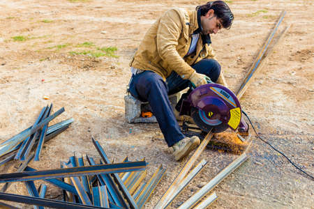 Iraqi worker using electrical saw to cut steel rods in Iraqi desert