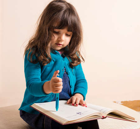 Samll girl inside studio with red copybook and blue pen in hand in hand