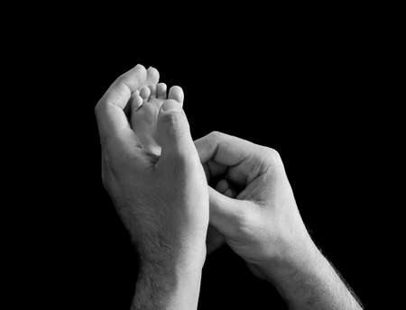 Newborn feet inside a his dad or mom hand isolated on black background