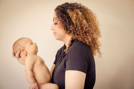 Brunette Mom playing with her newborn baby isloated on off white backgroundの写真素材