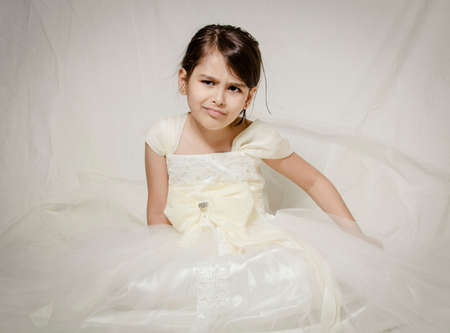 Small girl in bridal dress sitting isolated inside studioの写真素材