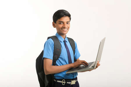 Indian school boy in uniform and using laptop on white background.の写真素材