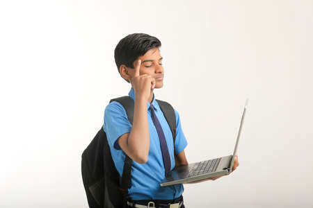 Indian school boy in uniform and using laptop on white background.の写真素材