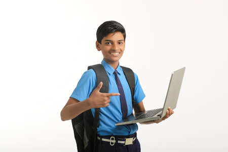 Indian school boy in uniform and using laptop on white background.