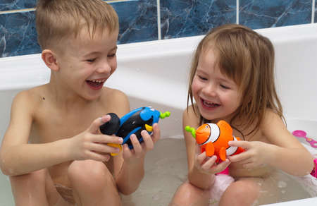 Boy and girl are plaing in bath with toy fishの写真素材