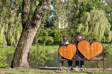 Woman and man are sitting on a bench with two hearts under  the treeの写真素材