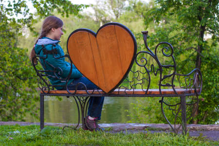 Young woman is sitting and waiting on a bench with big heart on itの写真素材