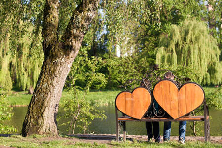 Woman and man are sitting on a bench with two hearts under  the treeの写真素材