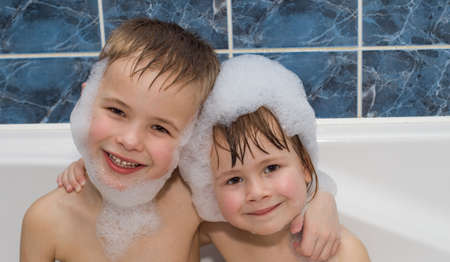 Two little children in a bathtub with shampoo foam on facesの写真素材