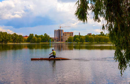 Man is rowing on a kayak boat on city lake on a sunny day