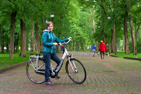 Young woman with a bicycle in the park green treesの写真素材