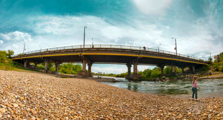 Little girl is playing at the river near big bridge in the city panoramaの写真素材