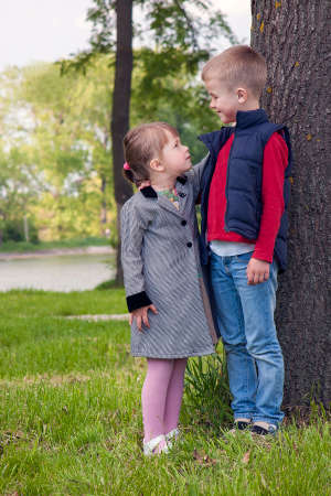 Little boy and girl on a sunny day standing on green grass near  tree looking at each otherの写真素材