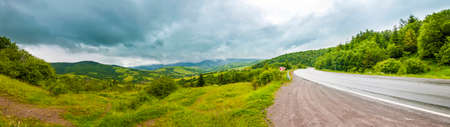 Road in mountains with dramatic sky and heavy clouds panoramaの写真素材