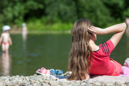 Young mother looking after her children on the bank of the river on summer sunny dayの写真素材