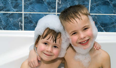 Two little children in a bathtub with shampoo foam on facesの写真素材