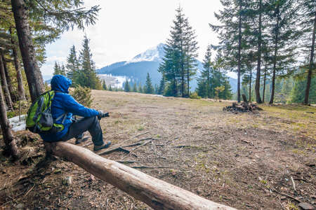 Lonely hiker traveler sitting on a log waching mountain sceneryの写真素材