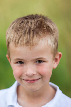 Portrait of a little smiling boy with golden blonde straw hair in sunny summer day on green blurred backgroundの写真素材