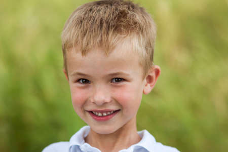 Portrait of a little smiling boy with golden blonde straw hair in sunny summer day on green blurred backgroundの写真素材