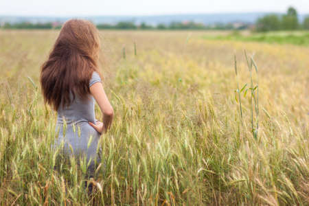Young woman with long brown hair standing in wheat field. Unity with nature concept.の写真素材