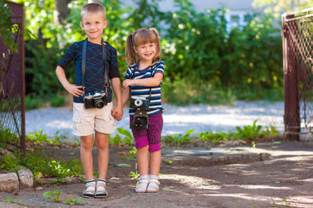 Little boy and a little girl wit two vintage cameras standing together holding handsの写真素材