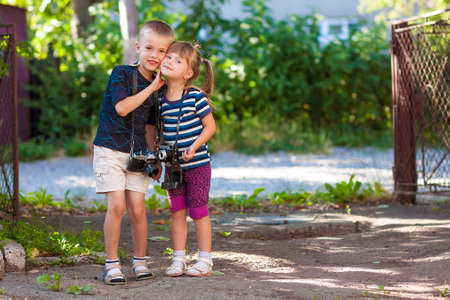 Little boy and a little girl wit two vintage cameras standing together holding handsの写真素材