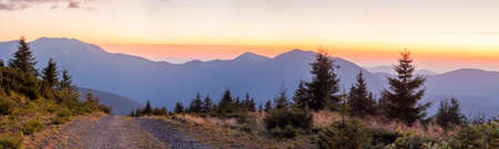 Panorama of sunset in Carpathian mountains with a gravel road in frontの写真素材