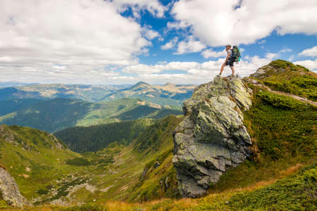 Hiker with a backpack standing o big stone in green rocky mountainsの写真素材