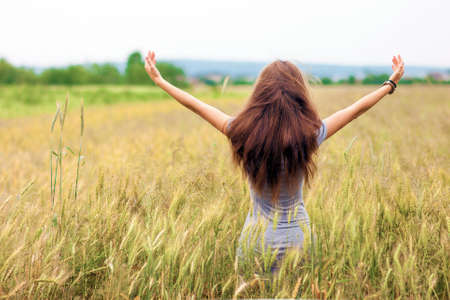 Young woman with long brown hair standing in wheat field raising hands. Unity with nature concept.の写真素材