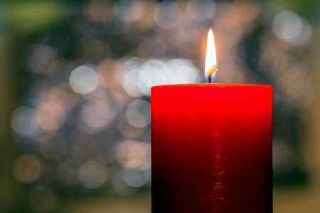 Candles light. Christmas candle burning at night. Abstract candle background. Golden light of candle flame. Closeup of a red candle with creamy bokeh background.の写真素材