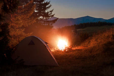 Hikers tent in mountains at evening with a bonfire with sparkles nearの写真素材