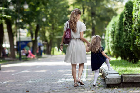 Rear view of young mother walking with little girl daughter in  beautiful summer park, wearing...