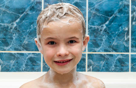 Adorable baby boy with shampoo soap suds on hair taking bath. Closeup portrait of smiling kid, health care and hygiene concept . Isolated on white and blue background with clipping path.の写真素材