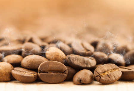 Brown coffee beans with white smoke vapour on yellow textured wooden board background close up.の写真素材