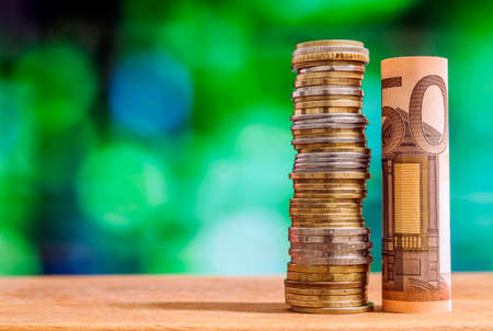Fifty euro rolled bill banknote, with euro coins on green blurred bokeh background.の写真素材