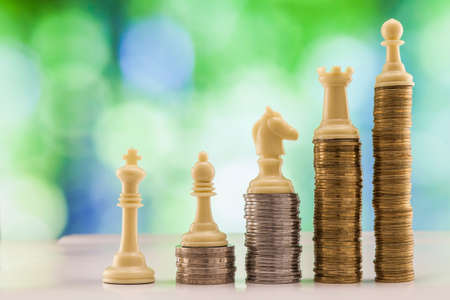 Growing coins stacks with green and blue sparkling bokeh background. Chess figures standing on coins meaning power and career growth. Financial growth, saving money, business finance wealth and success concept.の写真素材
