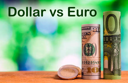 One hundred euro and one hundred US dollar rolled bills banknotes, with euro coins and american cents on green blurred bokeh background. Dollar vs Euro concept.の写真素材