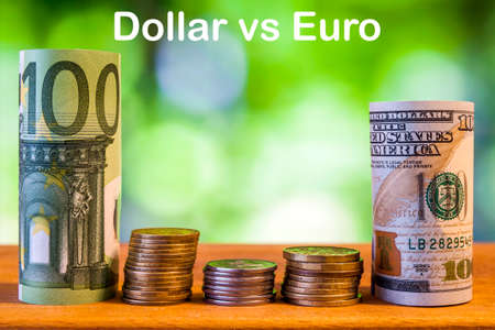 One hundred euro and one hundred US dollar rolled bills banknotes, with euro coins and american cents on green blurred bokeh background. Dollar vs Euro concept.の写真素材