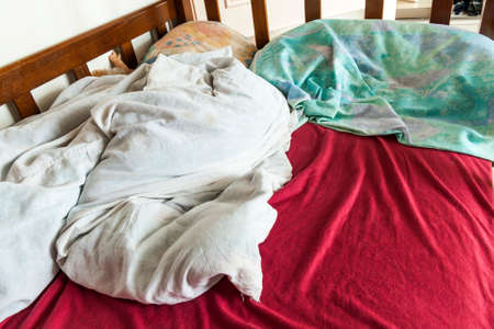 Unmade child bed with crumpled red and white bed linens and pillow.