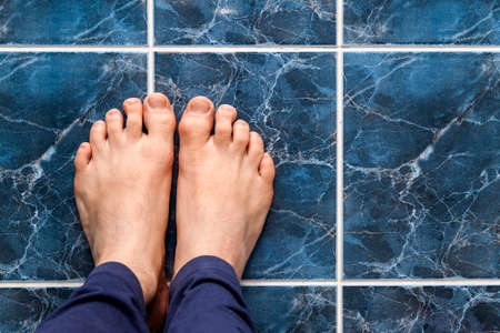 Young man crossing feet on square tiles. Veins in feet visible.の写真素材