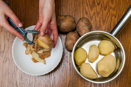 Detail of woman hands peeling fresh yellow potato with kitchen peeler, Food preparation concept.の写真素材