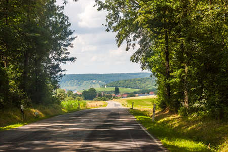 Asphalt country rural road in Germany through the green field and clouds on blue sky in summer dayの写真素材