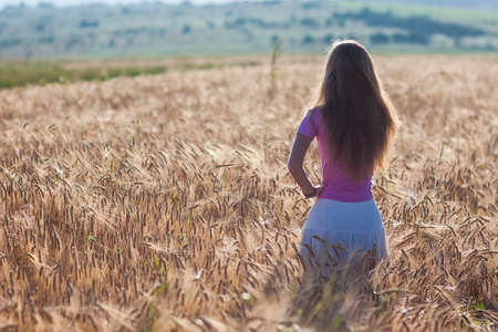 Happy young girl in golden wheat field. Young woman enjoying nature and sunlight in straw field. Unity with nature concept.の写真素材